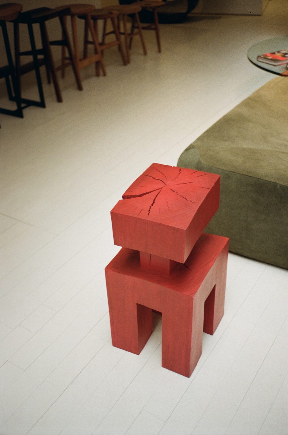 Red carved wood stool on a white floor, bar stools and a sofa behind