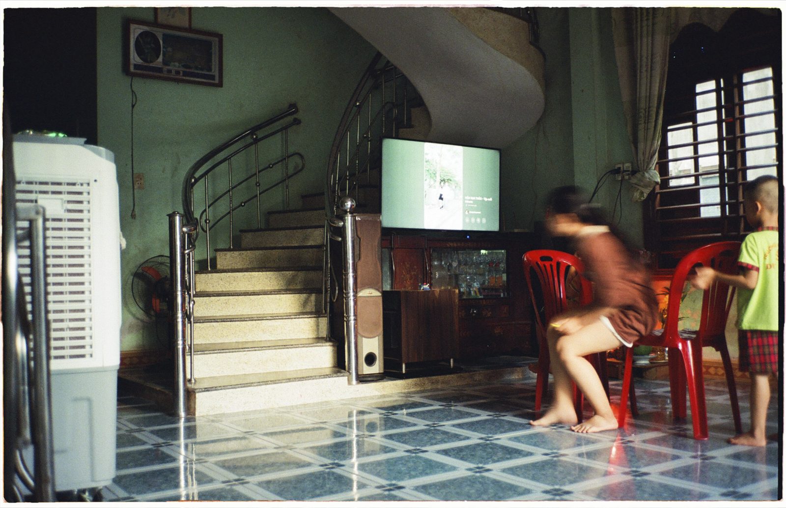 Home interior with a spiral staircase, red plastic chairs and children watching television